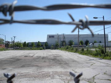 Close-up of barbed-wire fence with an industrial building in the background