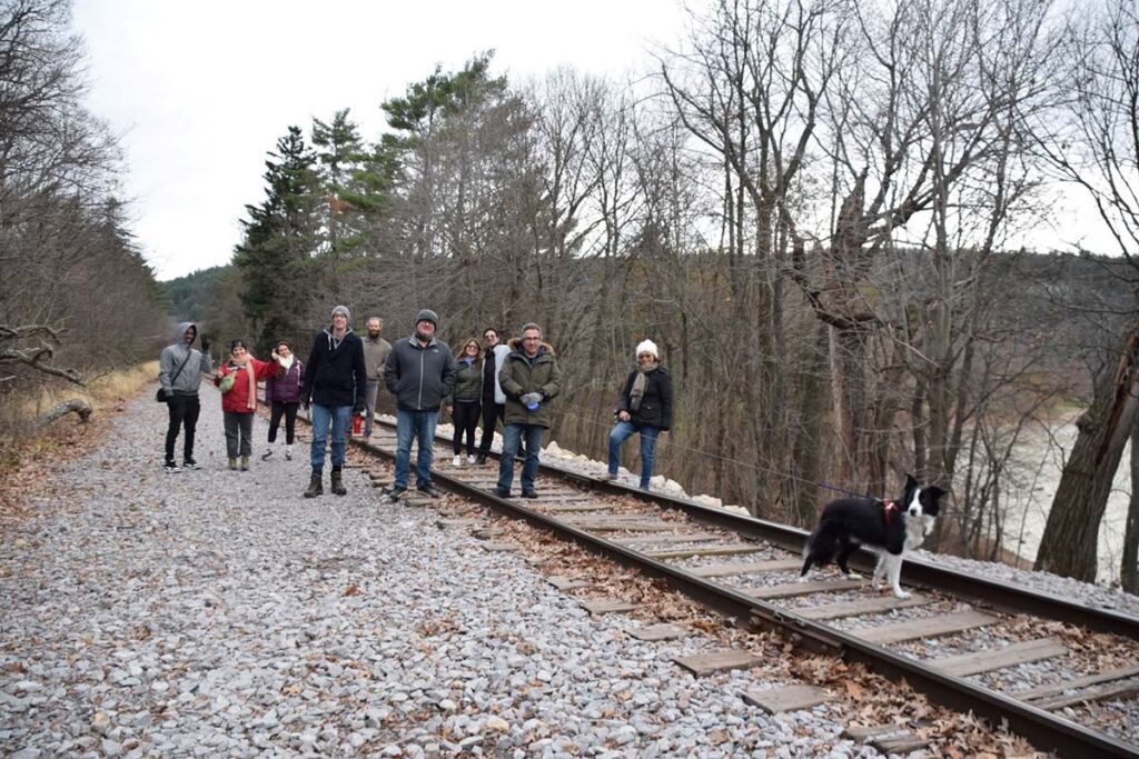 Wide-angle group photo along railroad tracks, with a border collie leading the way