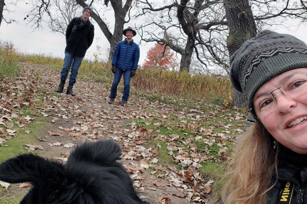 Selfie with three people standing on a hiking trail, with one person close up and the other two in the background