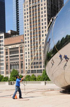 Person using a long pole with a brush on the end to clean the Chicago bean sculpture