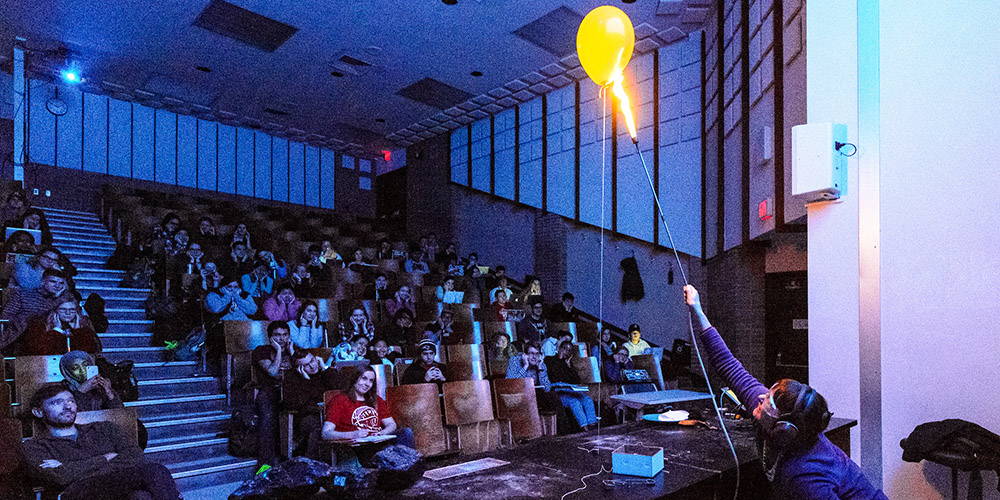 A professor puts a flame on a helium balloon during a lecture