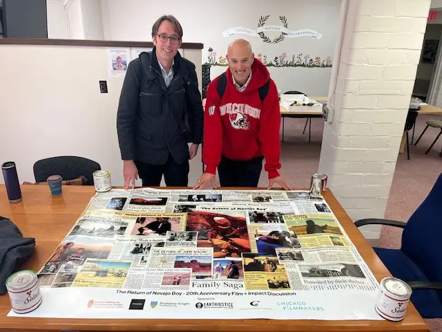 Will Brockliss and James Spitz standing over a poster-sized collage of newspaper clippings