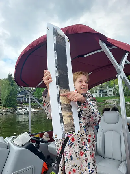 Sissel Schroeder standing on a pontoon boat, giving a presentation about dugout canoes