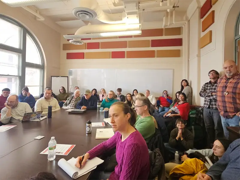 About 30 people sitting a conference room in Science Hall, intently watching a lecture